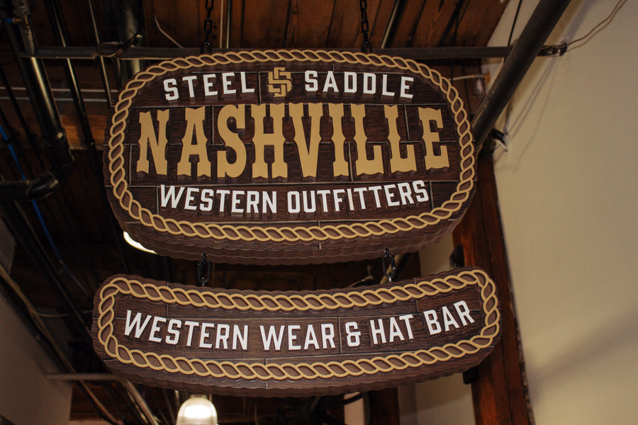 Hanging Steel & Saddle Nashville Western Outfitters sign reading Western Wear & Hat Bar