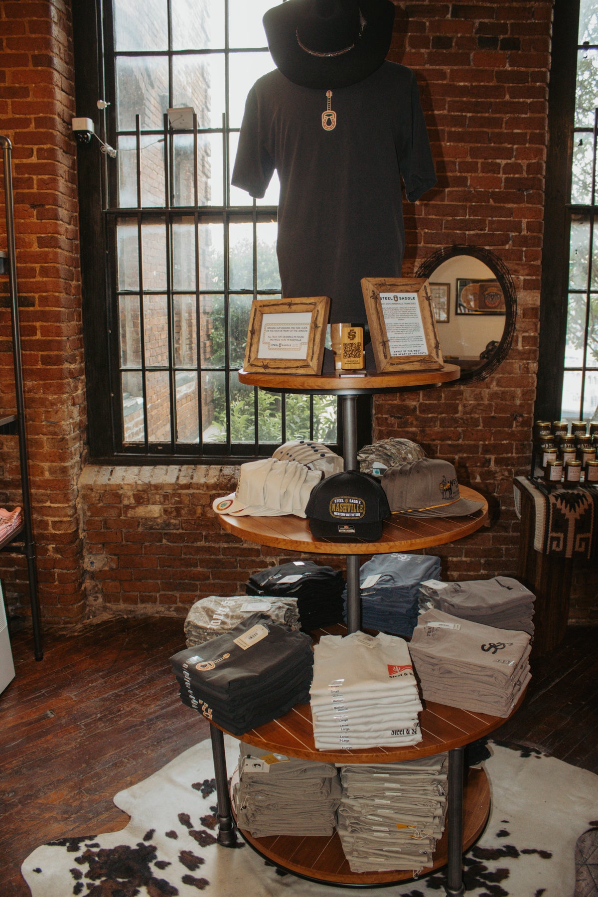 Folded Steel & Saddle tees and a hat on a display table by the shop window