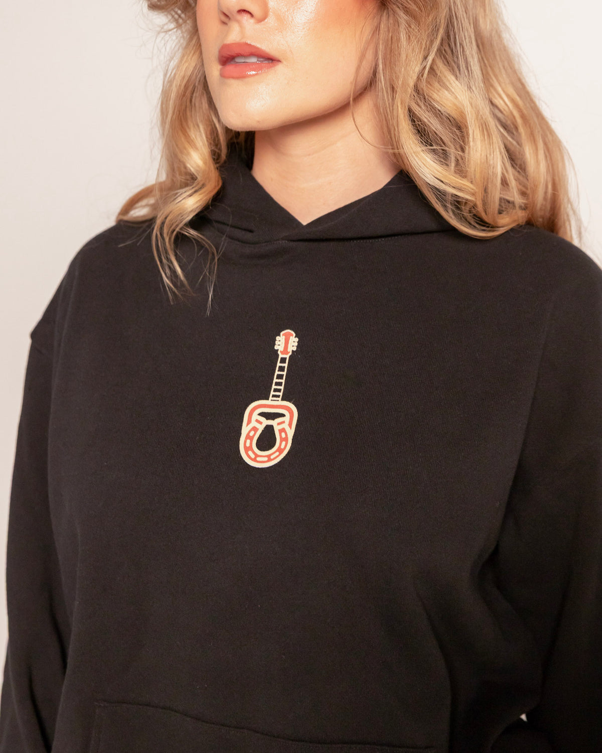 Broadway Hoodie in faded black, close-up of the guitar and horseshoe chest print