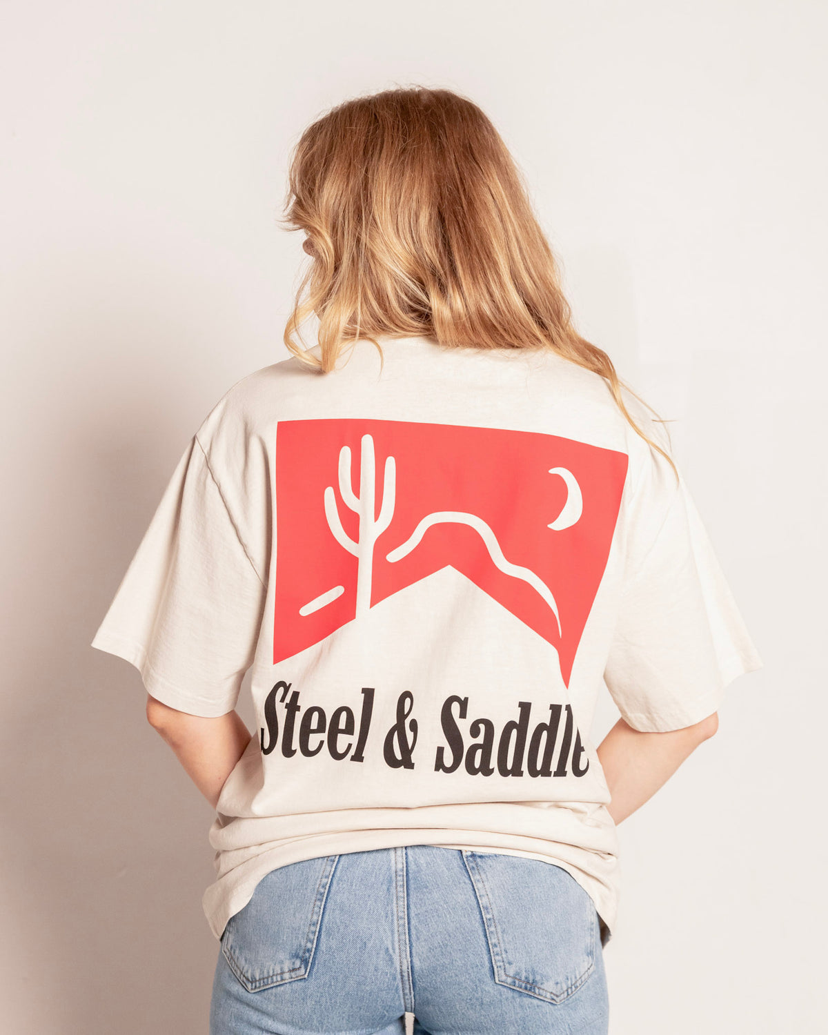 Cowboy Killer Tee in faded bone on model, back view with the red pack, cactus and moon over Steel & Saddle lettering