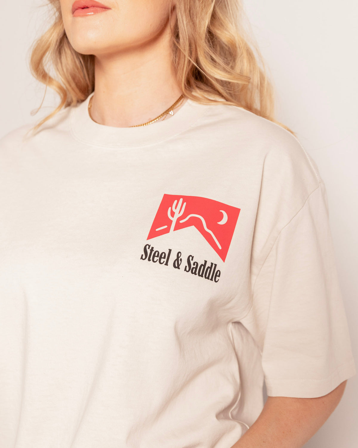 Cowboy Killer Tee in faded bone, close-up of the small red pack chest print