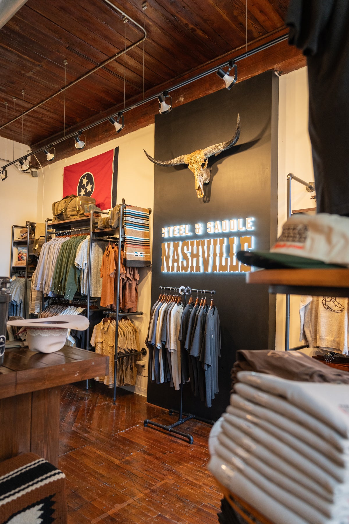Inside Steel & Saddle in Marathon Village, Nashville: the lit Steel & Saddle Nashville sign under a longhorn skull, racks of western shirts and a Tennessee flag