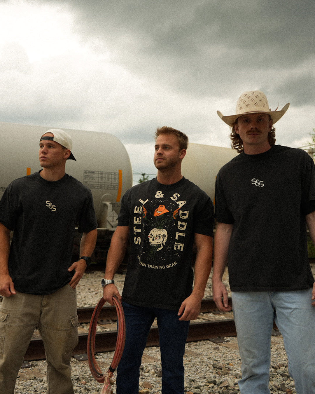 Three men standing on train tracks with a cloudy sky in the background