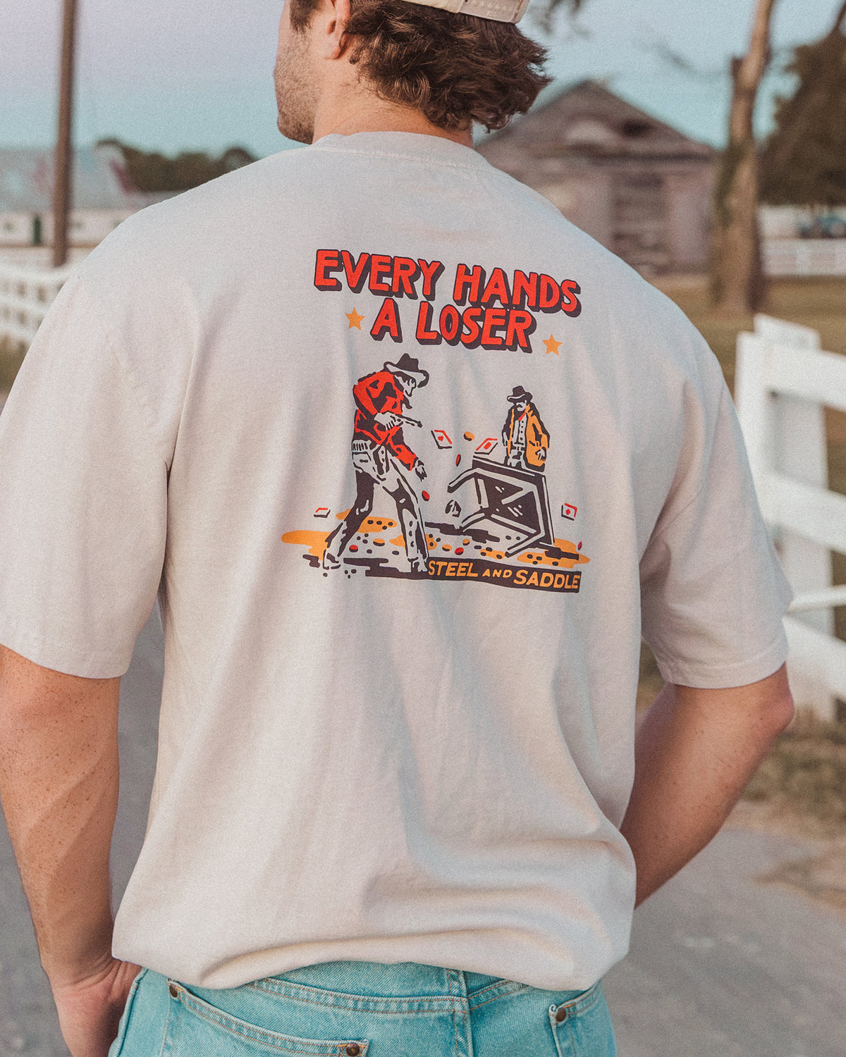 Gambler Tee in faded bone worn outdoors, back print of a cowboy flipping a poker table under Every Hands a Loser