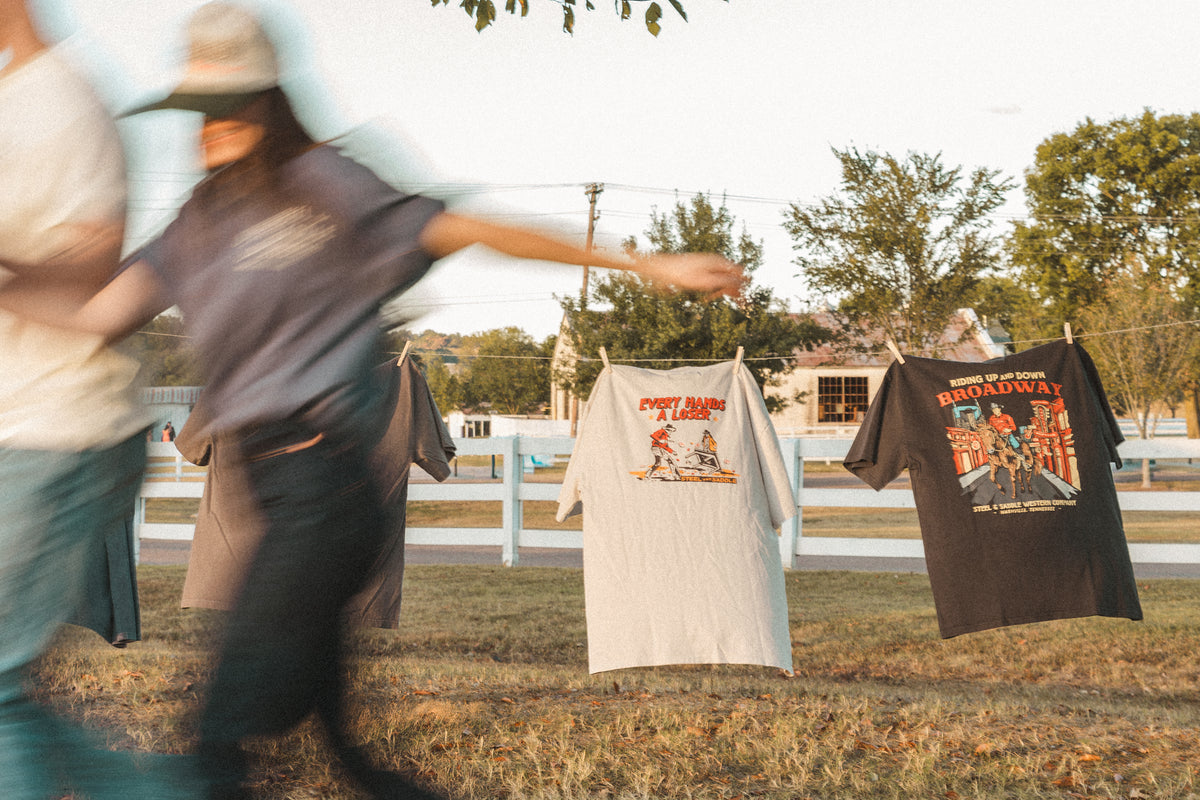 Steel & Saddle tees hanging on a clothesline as two people run past