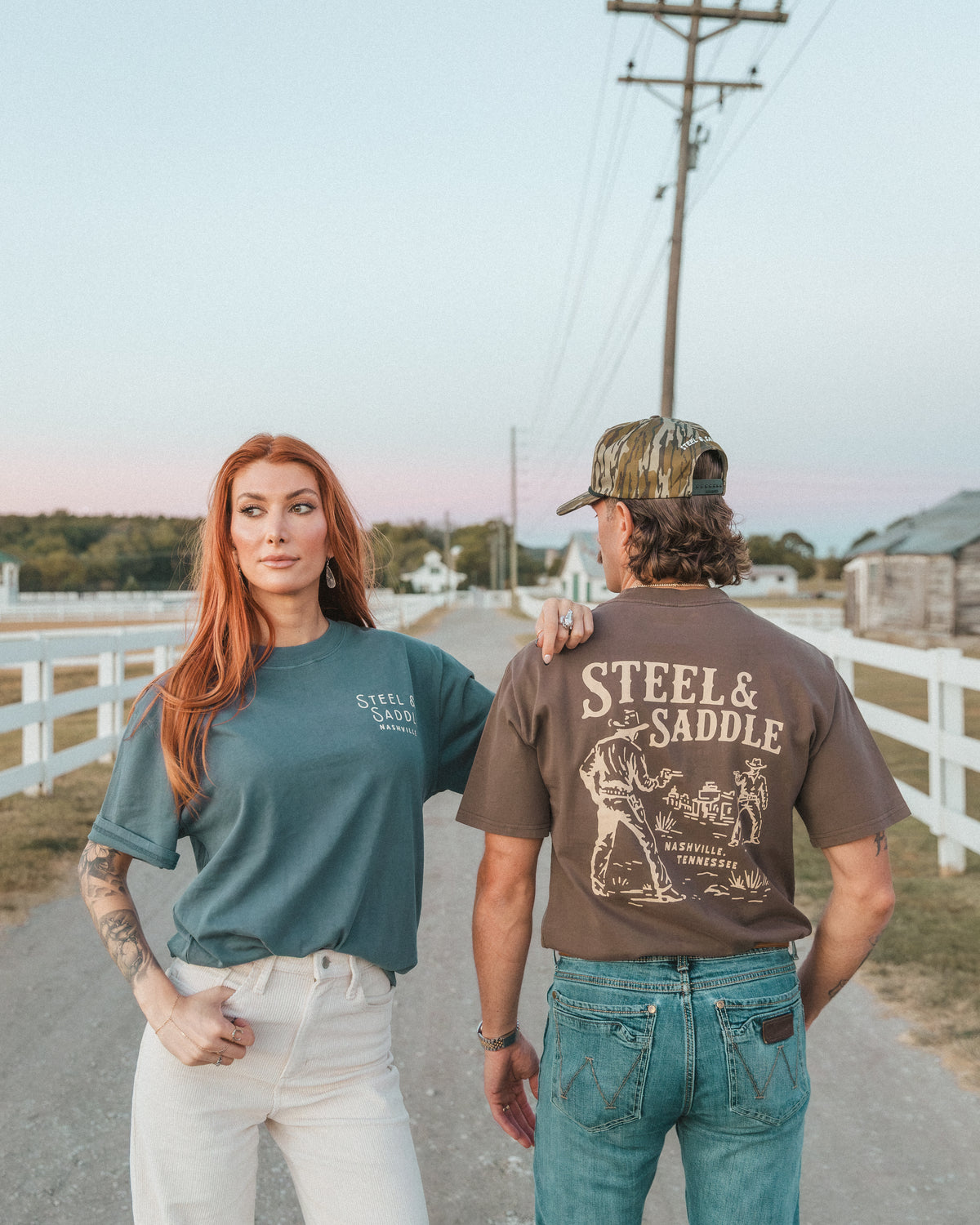 Woman in a faded teal tee beside a man showing the Lever Action Tee back print on a country road
