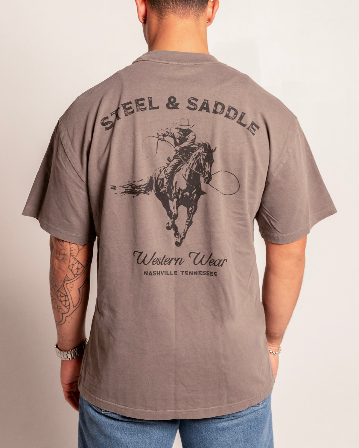 Lever Action Tee in faded grey on model, back view with the roping cowboy under arched Steel & Saddle lettering