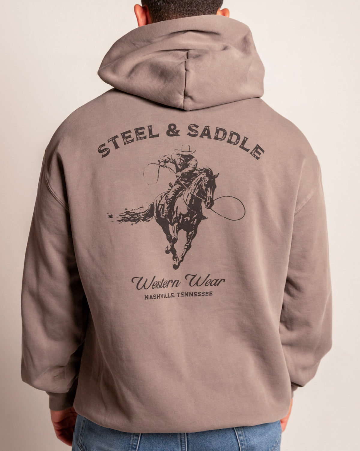 Lever Action Hoodie in faded grey on model, back view with the roping cowboy under arched Steel & Saddle lettering