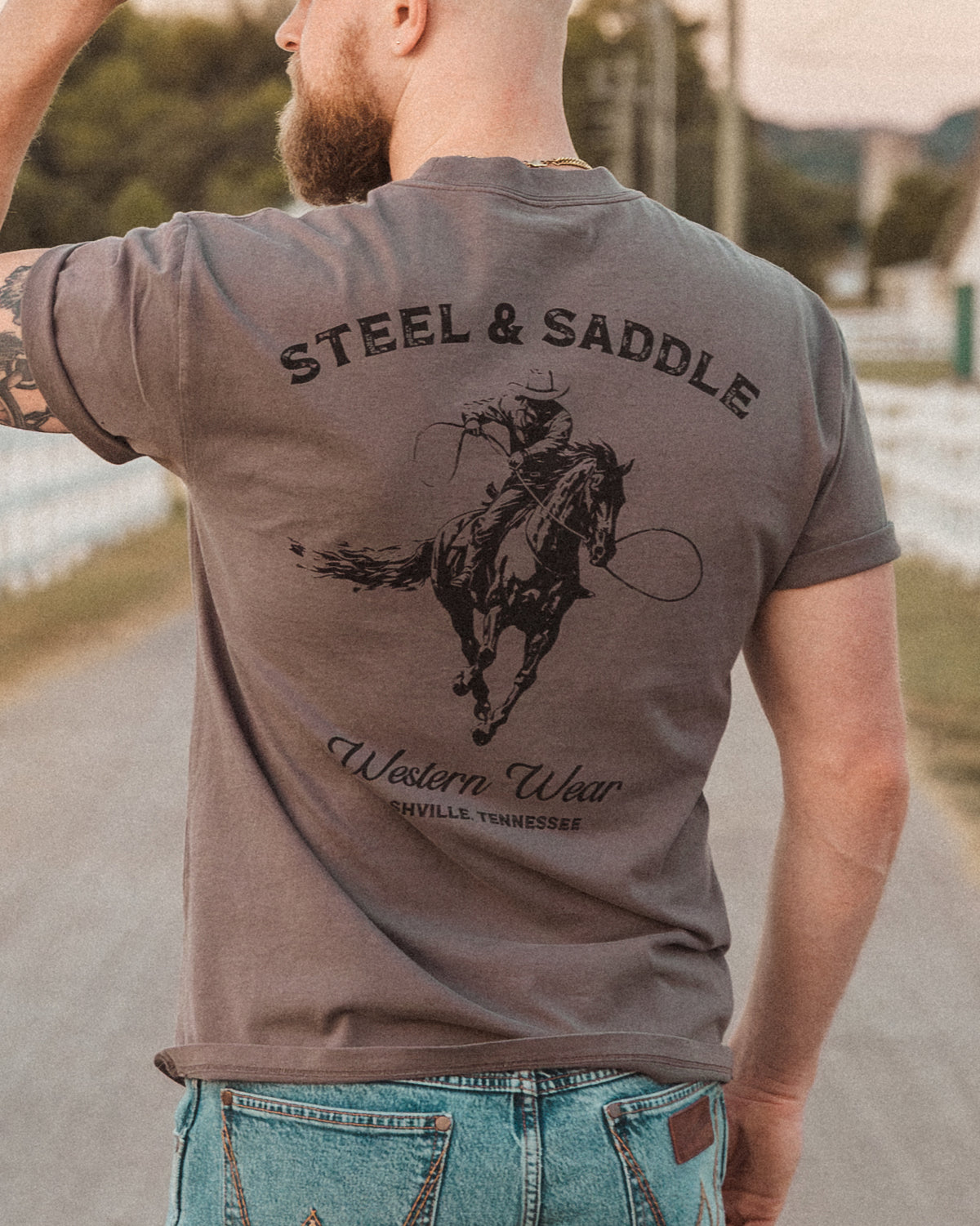 Lever Action Tee in faded grey worn outdoors, back print of a roping cowboy under arched Steel & Saddle lettering