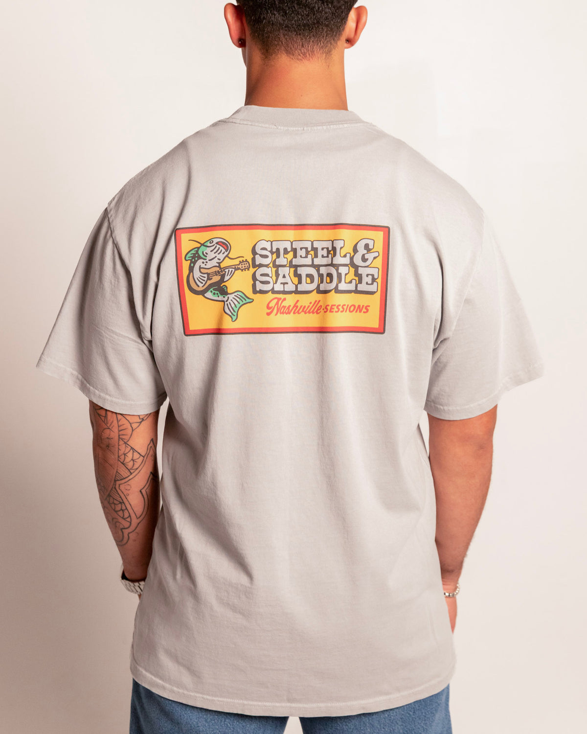 Nashville Sessions Tee in faded storm on model, back view with the catfish playing guitar on an orange patch