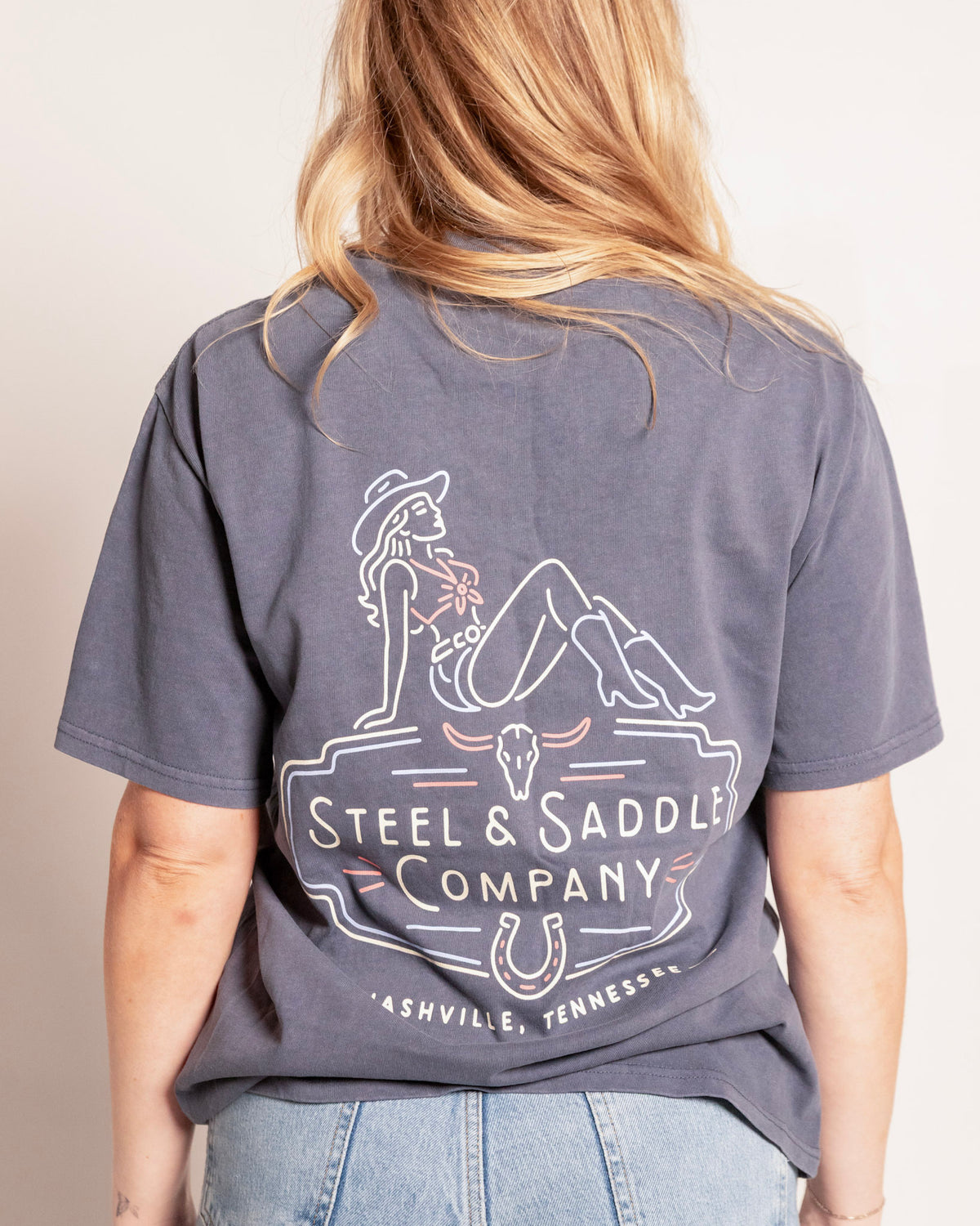 Music City Neon Tee in faded indigo on model, back view with the neon cowgirl on a Steel & Saddle Company sign