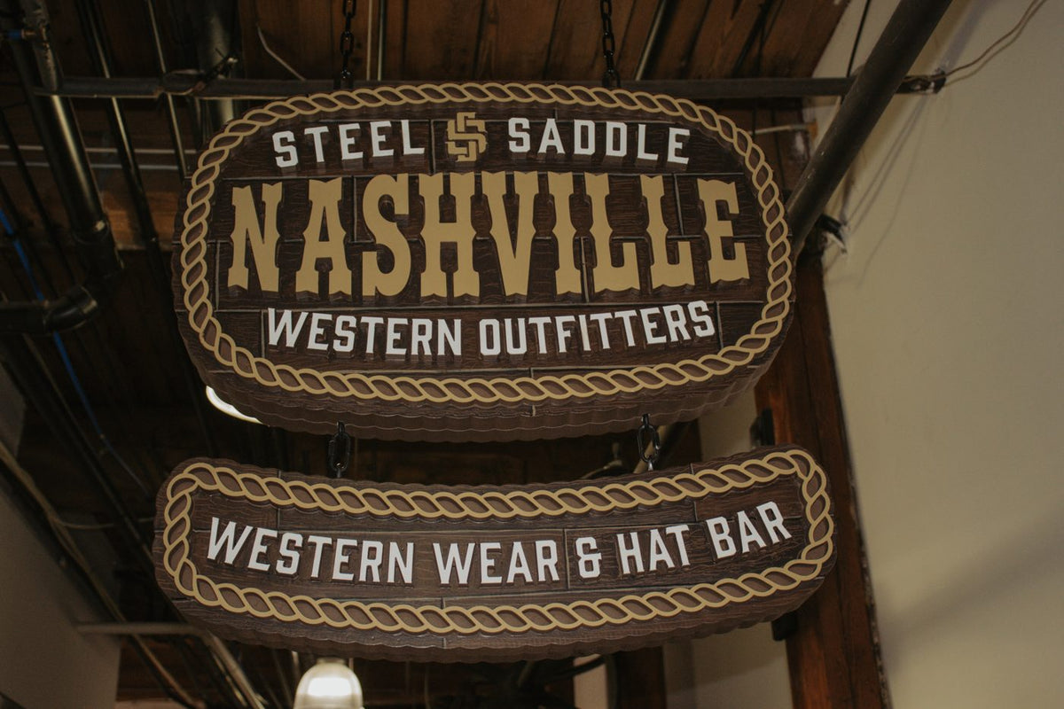 Hanging Steel & Saddle Nashville Western Outfitters sign reading Western Wear & Hat Bar